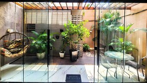 A glass-enclosed patio with a swing chair, potted plants, and a table with chairs. - Morumbi Triplex House with Jacuzzi (São Paulo)
