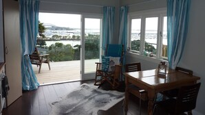 A room with a wooden dining table, chairs, a rocking chair, a large window with curtains, and a view of a marina. - Million Dollar View! (Auckland)