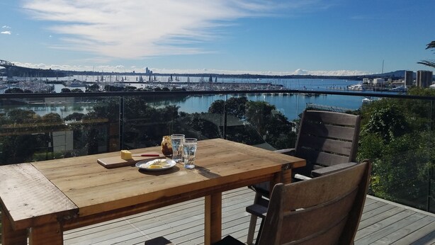 A wooden table with chairs on a balcony overlooking a marina with boats and a bridge in the distance. - Million Dollar View! (Auckland)