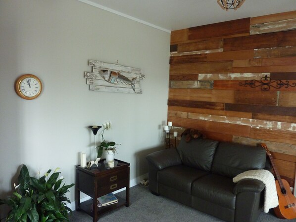 Un salon avec un lambris en bois, une horloge, une petite table avec une plante, un canapé et une guitare.