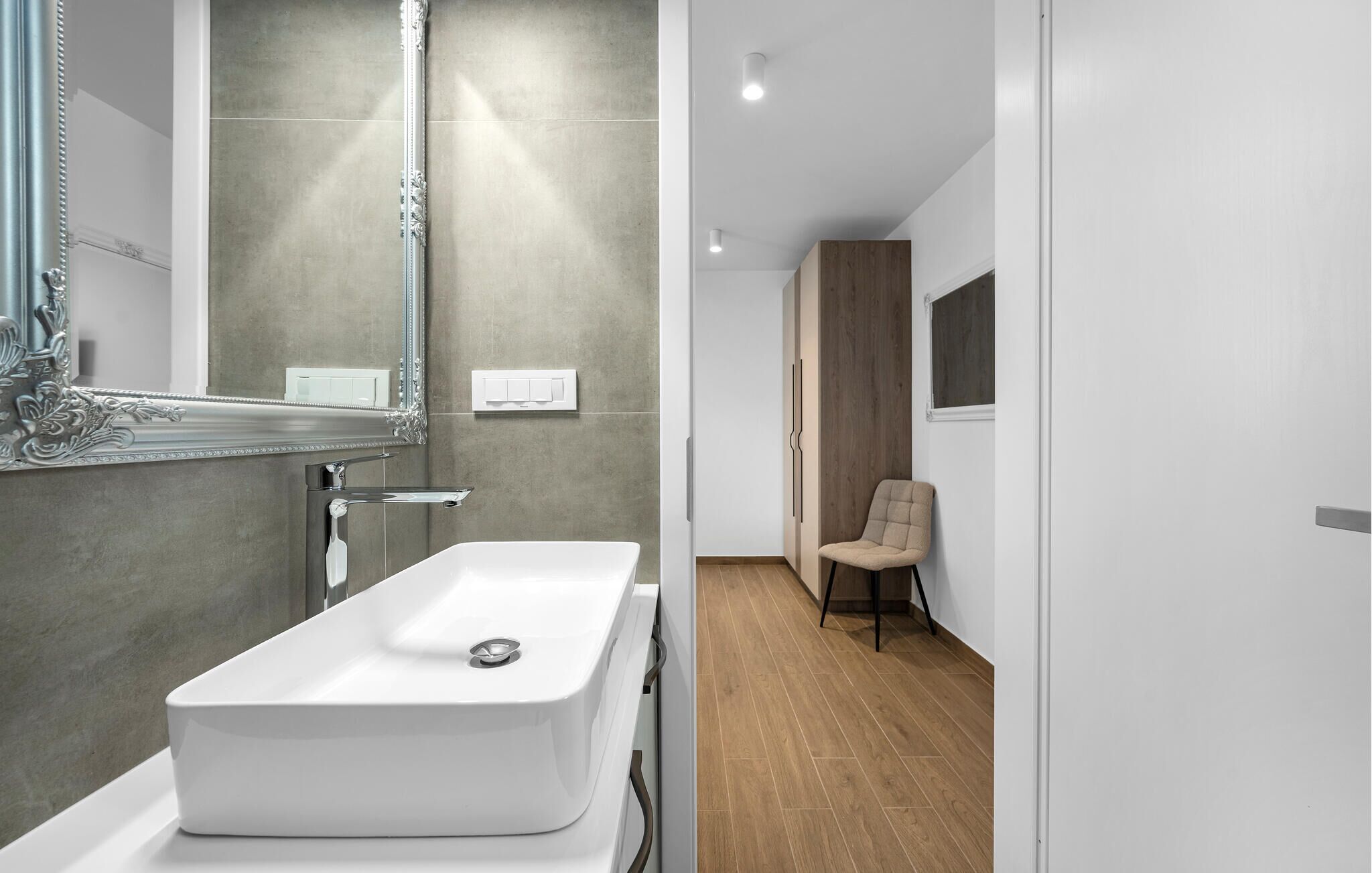 A modern bathroom with a large mirror, a white sink, and a wooden floor.