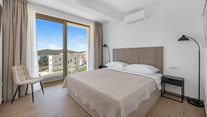 Een hotelkamer met een bed, een stoel, een bureau, een lamp en uitzicht op gebouwen en heuvels.