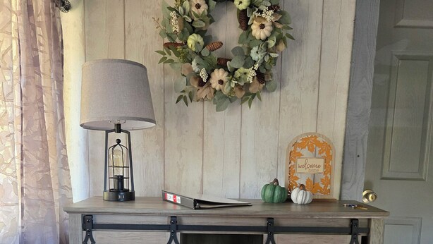 A rustic wooden console table with a decorative wreath, a lamp, and a welcome sign.
