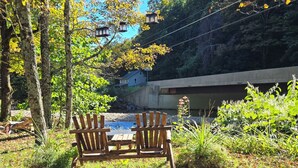 A wooden bench with a table in a natural setting with trees and a concrete structure in the background.