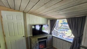 A cozy living room with a fireplace, a flat-screen TV, and a large window with curtains.