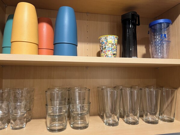 Une étagère avec des gobelets en plastique de couleurs vives et des verres transparents.