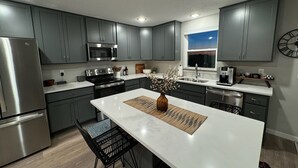 Una cocina moderna con armarios grises, electrodomésticos de acero inoxidable, una isla central con un jarrón y una ventana con vistas.