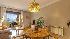 A modern living room with a round wooden dining table, a sofa, and a large window overlooking a balcony.