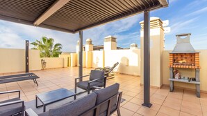 An outdoor patio with a covered seating area, a barbecue grill, and a tiled floor.