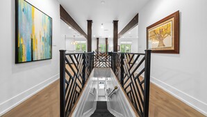 Una escalera moderna con barandilla de vidrio, paredes blancas y suelo de madera.