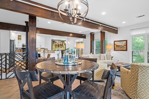 A spacious living area with a round wooden dining table, dark wooden chairs, a sofa, and a patterned armchair.