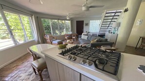 A kitchen with a central island, a dining area with wicker furniture, and a staircase leading to an upper level.