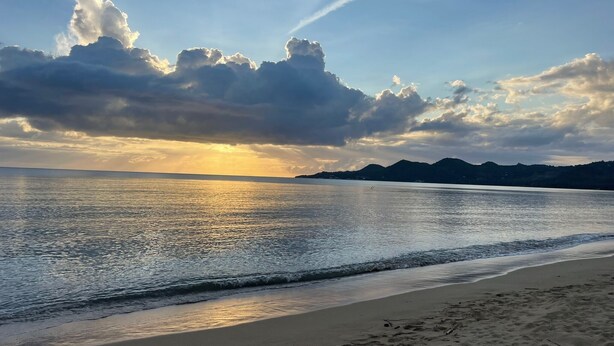 A beach with a calm sea, a clear sky, and distant mountains.