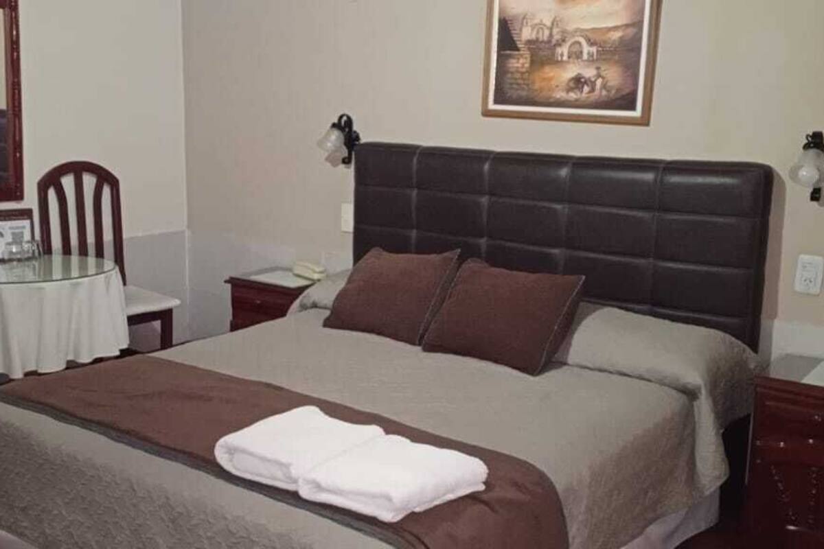 Een netjes ingerichte slaapkamer met een groot bed, een klein rond tafeltje, twee stoelen en een ingelijst schilderij aan de muur.