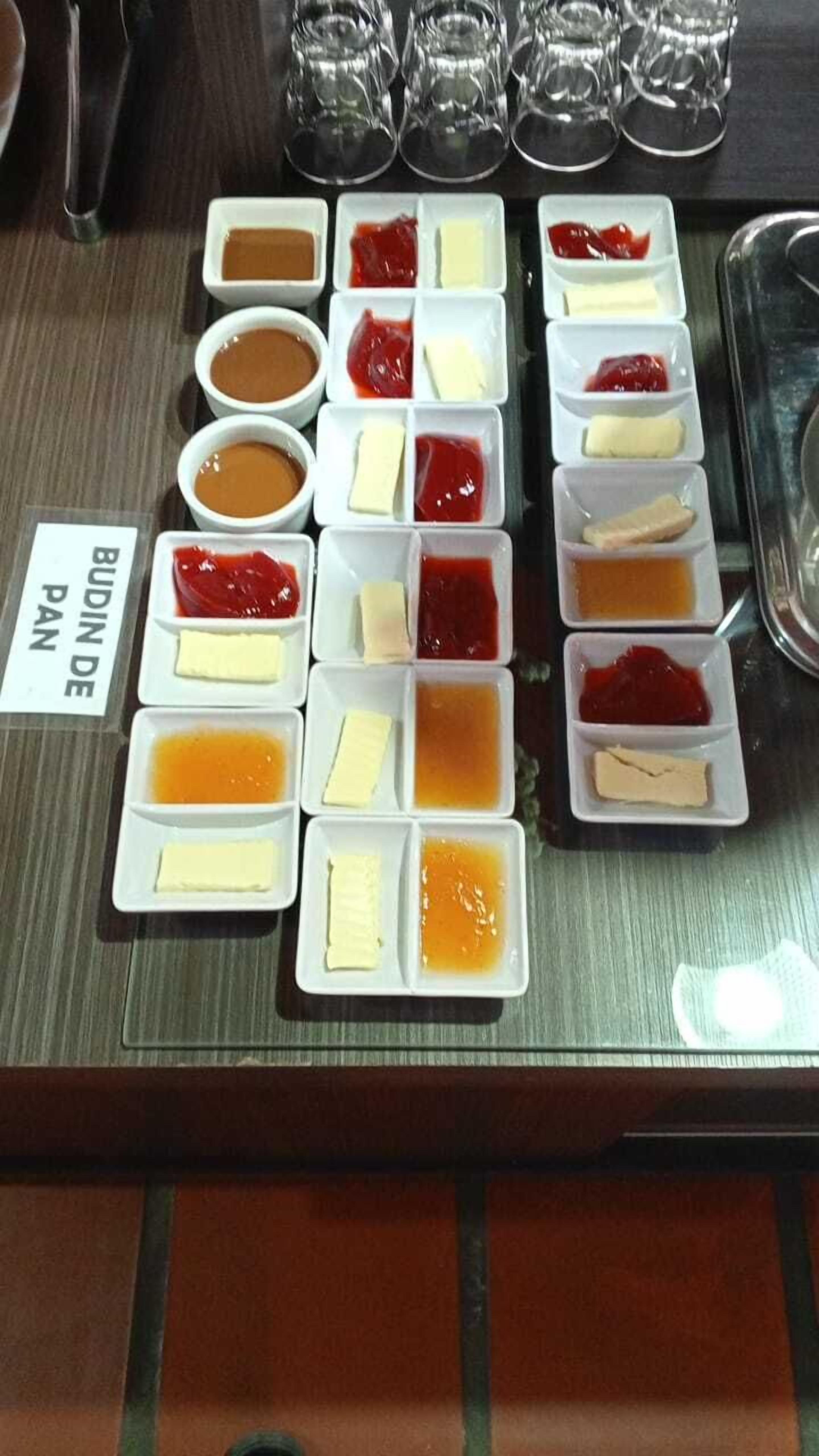 A buffet with various food items and condiments arranged in white square dishes.