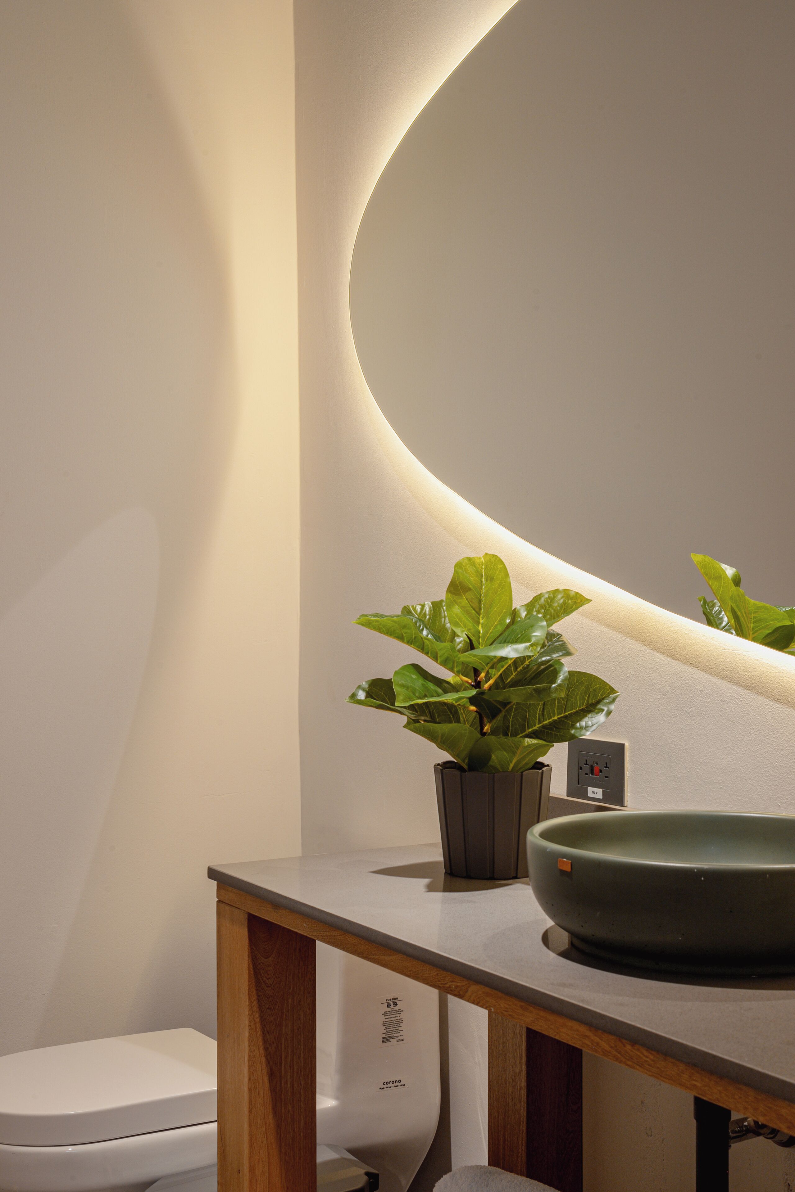 A modern bathroom with a toilet, a sink with a green basin, and a potted plant.