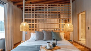 A neatly made bed with a tray of coffee and a mug, a wooden headboard, and a large window with curtains.