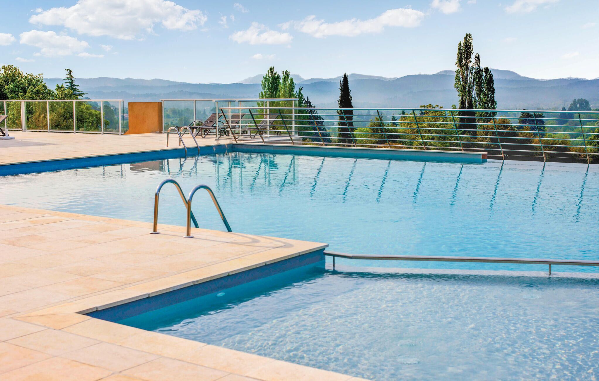 Une piscine à l’eau d’un bleu cristallin, entourée d’une terrasse carrelée et de rampes en métal.