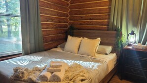 A wooden log cabin bedroom with a bed, pillows, a blanket, and a bedside table with a lantern. - Charming 3-bedroom cabin in Eucha with WiFi and FirePit (Eucha)