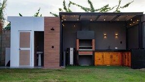 Una cocina exterior moderna con horno empotrado y pileta, rodeada por un patio cubierto con luces colgantes.
