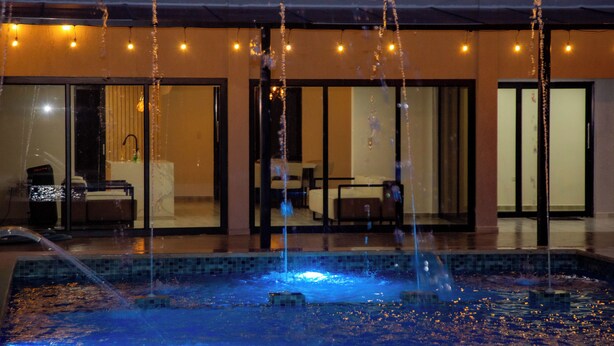 Un hotel moderno con piscina que incluye chorros de agua e iluminación con luces colgantes.