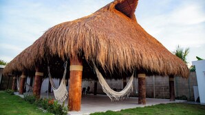 Estructura con techo de paja, una hamaca y zona de piscina.