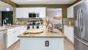 A modern kitchen with white cabinets, granite countertops, stainless steel appliances, and a central island. - 5BR Retreat: Arcade, Cowboy Pool & Volleyball Oasis in Huge Backyard (Round Rock)