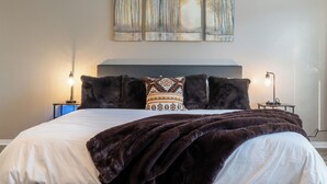 A neatly made bed with a dark brown blanket, a patterned pillow, and a headboard. There are two bedside lamps on either side of the bed. - 5BR Retreat: Arcade, Cowboy Pool & Volleyball Oasis in Huge Backyard (Round Rock)