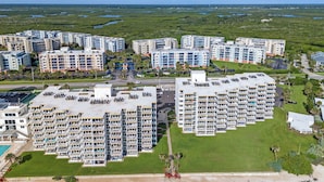 A high-rise hotel with multiple balconies, a parking lot, and a view of the surrounding landscape.