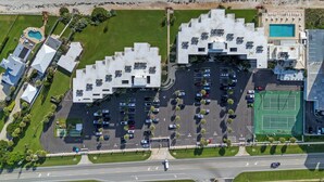 An aerial view of a hotel with a parking lot, a tennis court, and a pool area.
