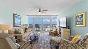 A living room with a view of the ocean, a ceiling fan, and a television.