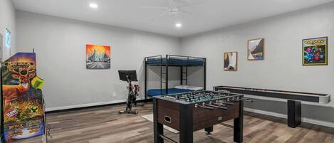 A room with a foosball table, a bunk bed, a stationary bike, and a large poster of a video game.