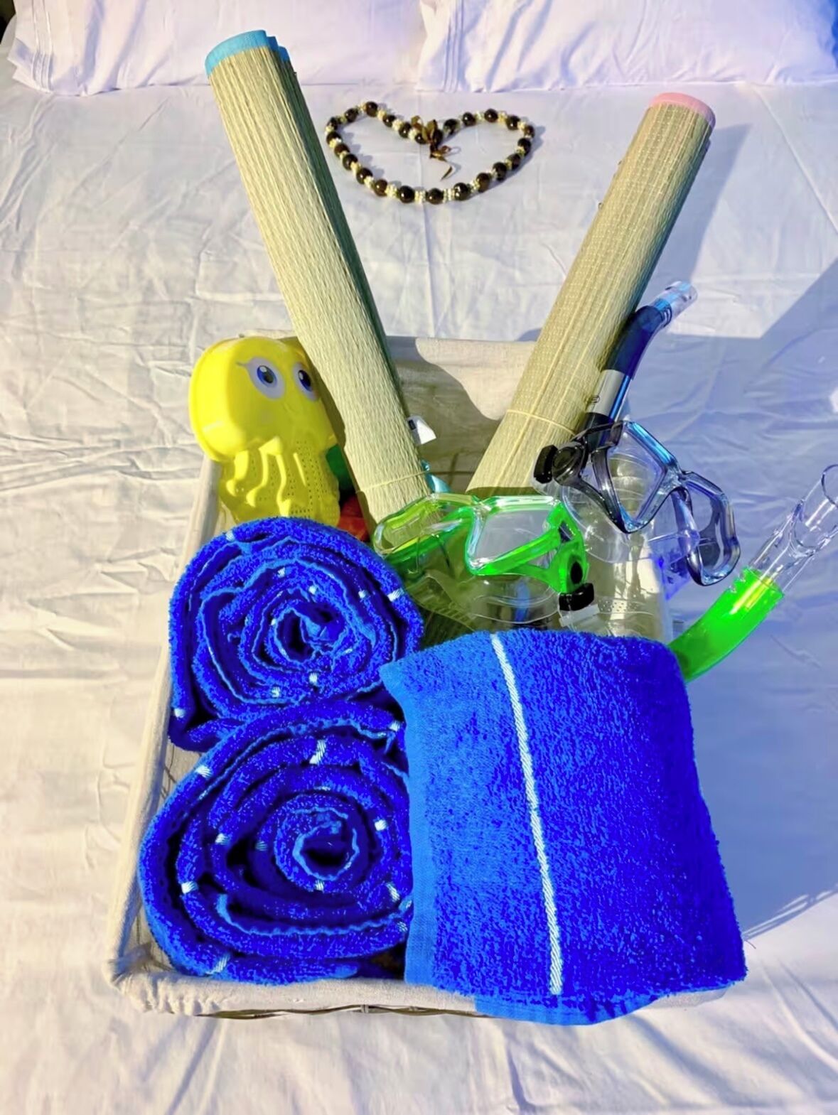 A tray with a yellow rubber duck, rolled blue towels, a beaded necklace, and a pair of scissors.