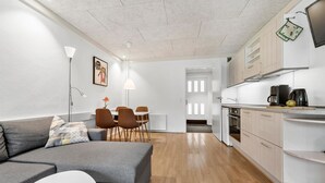 Un appartement moderne avec un canapé gris, une table à manger avec des chaises, une cuisine avec des meubles blancs et une grande fenêtre.
