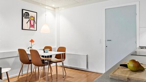 Une cuisine moderne avec une porte blanche, un coin repas avec une table et des chaises, et un fruit posé sur le comptoir.