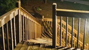 Eine Holztreppe führt zu einer Terrasse mit Blick auf einen Wald und eine Straße im Hintergrund.
