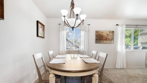A dining room with a round wooden table, white chairs, a chandelier, and a painting on the wall.