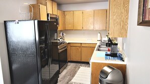 A kitchen with wooden cabinets, a black refrigerator, a sink, and a stainless steel trash can.