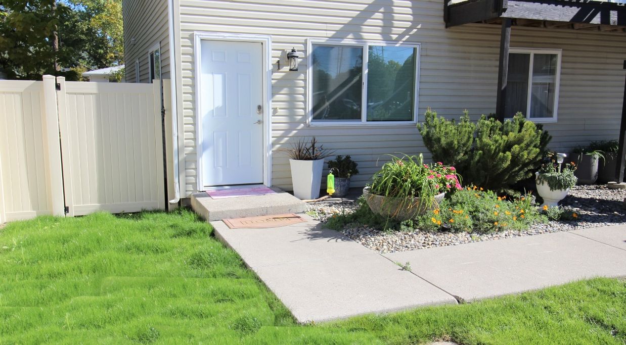 Une maison d’habitation avec un jardin devant, une clôture en bois, une porte et des plantes en pot.