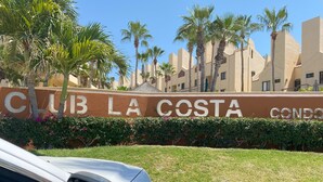 Schild für Club La Costa mit freiem Blick auf die Architektur des Gebäudes und umliegende Palmen.