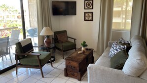 Ein Wohnzimmer mit einer Couch, Sesseln, einem Couchtisch, einem Fernseher und einem Balkon mit Blick.