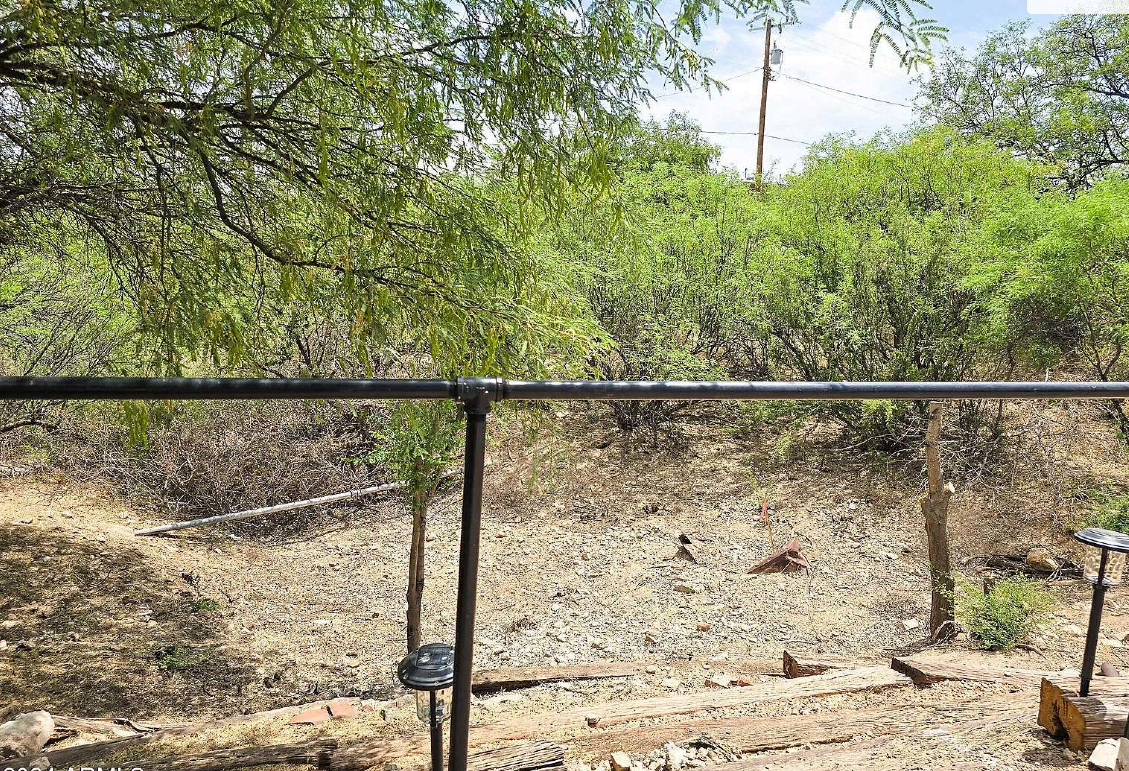 A fenced outdoor area with a dirt ground, wooden logs, and sparse vegetation.