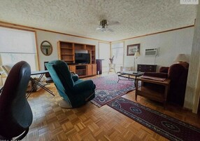 Una sala de estar con sofá, sillón, televisor y ventilador de techo.