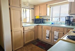 Una cocina con armarios de madera, un microondas, una estufa y un ventanal con persianas.