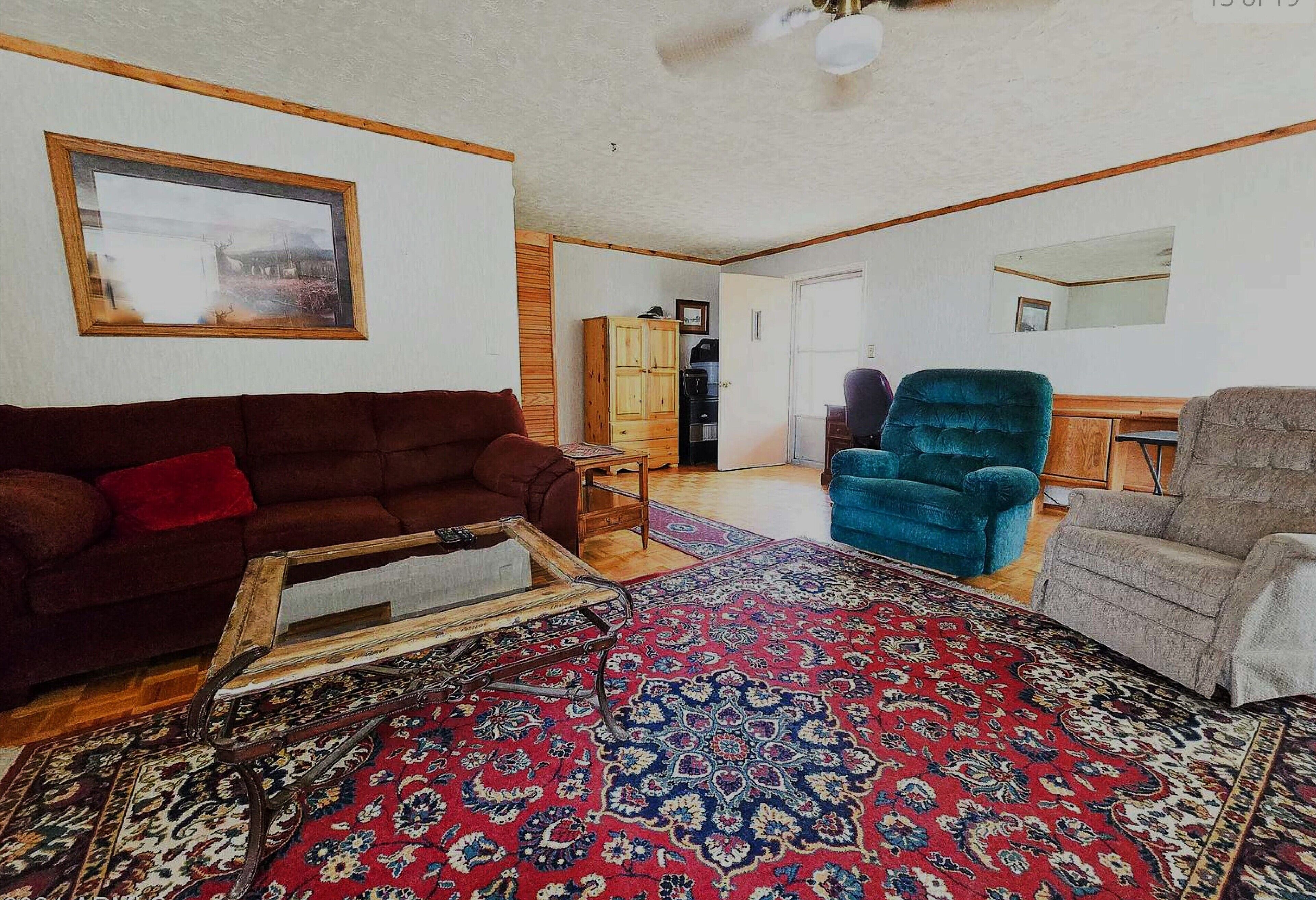 Ein Wohnzimmer mit einem braunen Sofa, einem blauen Sessel und einem grauen Sessel. Es gibt ein Holzschrank und einen kleinen Tisch.
