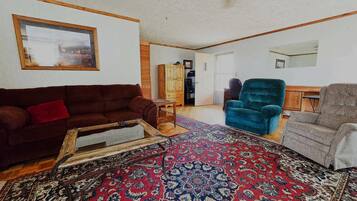 Ein Wohnzimmer mit einem braunen Sofa, einem blauen Sessel und einem grauen Sessel. Es gibt ein Holzschrank und einen kleinen Tisch.