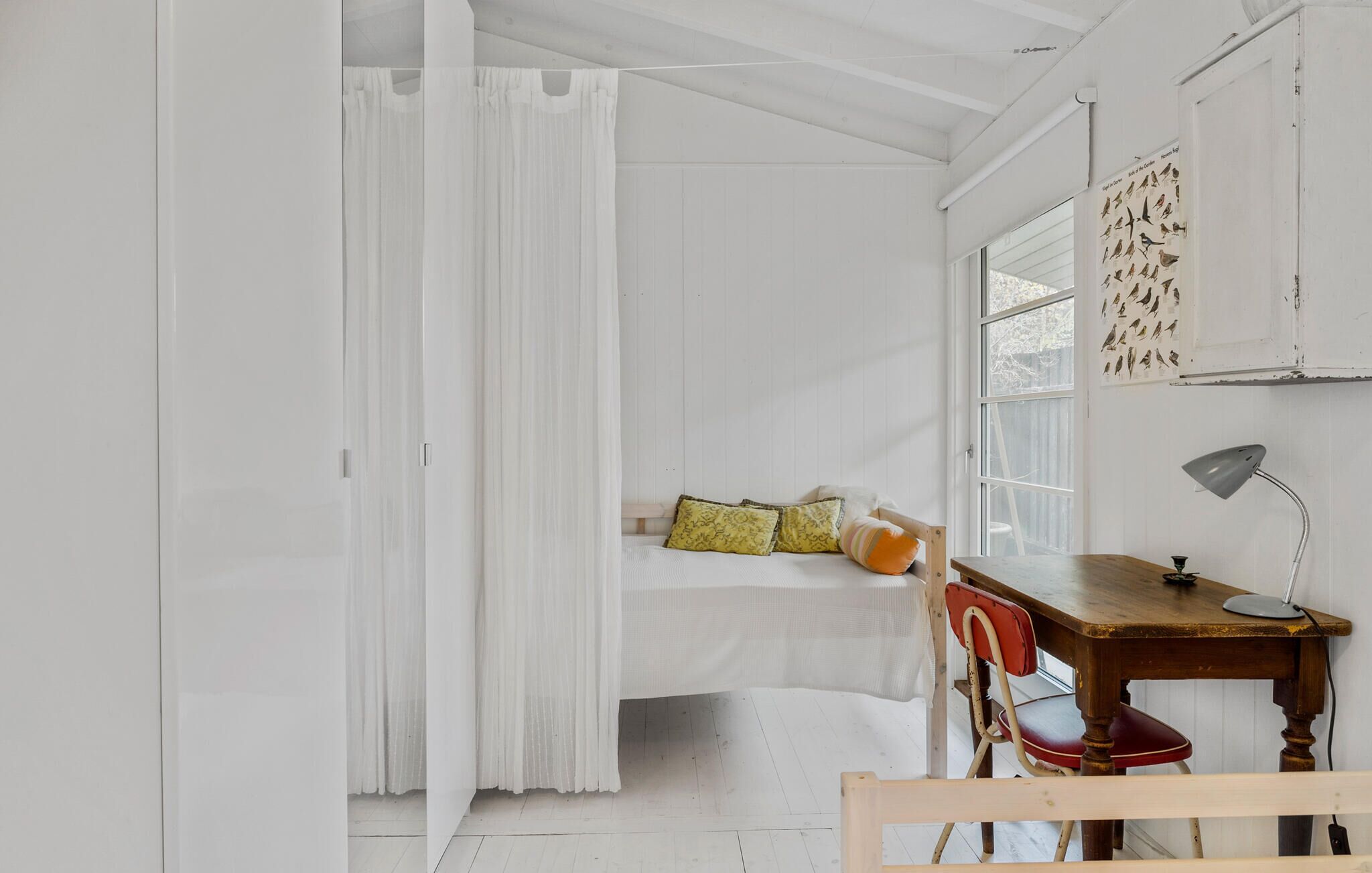 Una habitación con cama, escritorio, silla y ventana con estampado de pájaro.