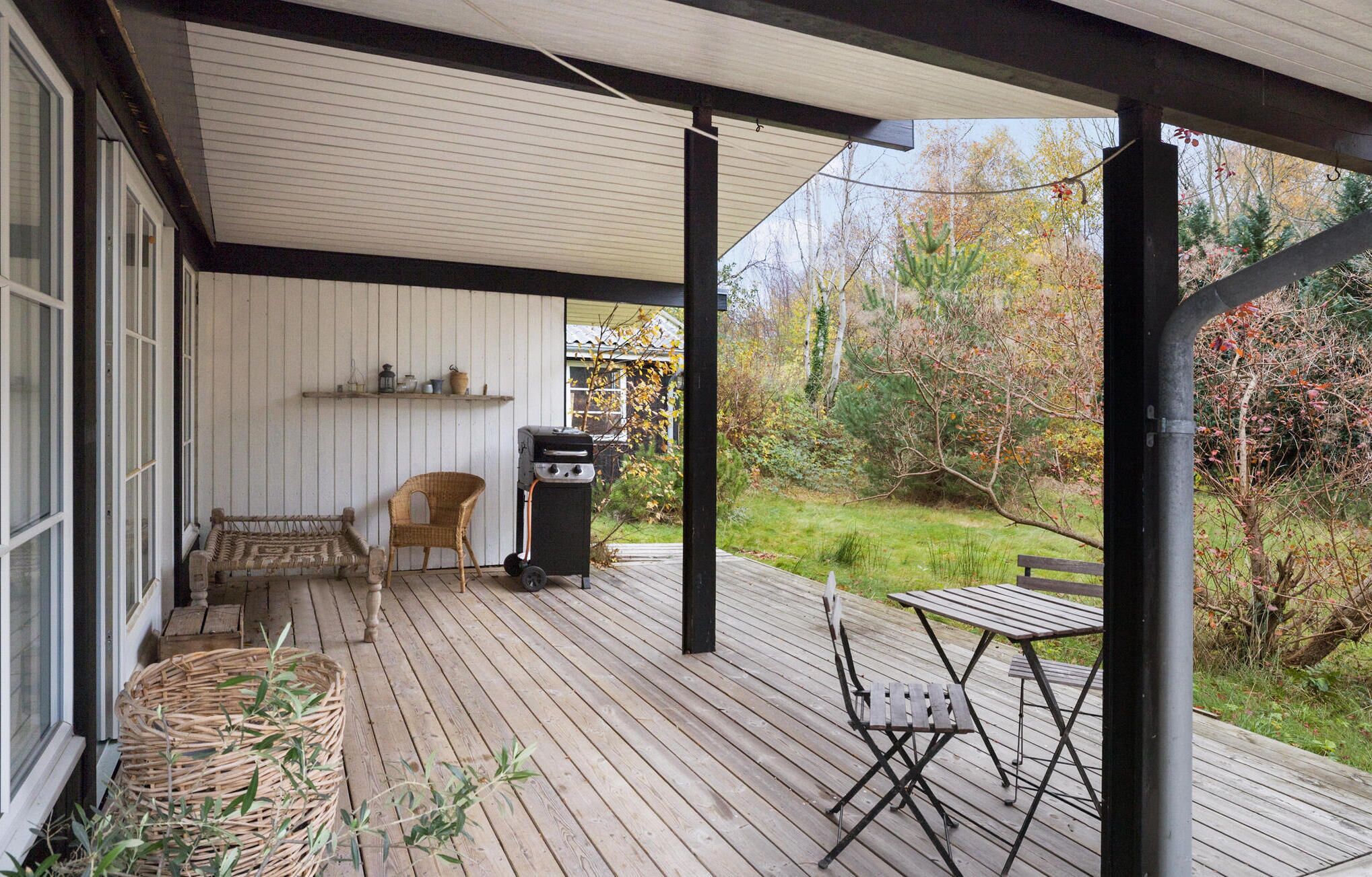 Eine überdachte Terrasse im Freien mit Grill, Korbmöbeln und Blick auf den umliegenden Garten.