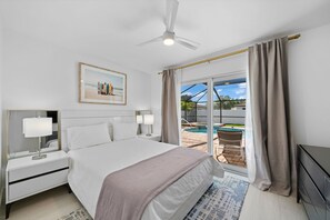 A modern hotel room with a large bed, a ceiling fan, a framed picture on the wall, and a view of an outdoor swimming pool.