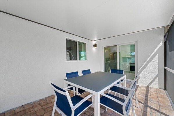 A patio with a table and chairs, a glass door leading inside, and a white wall.